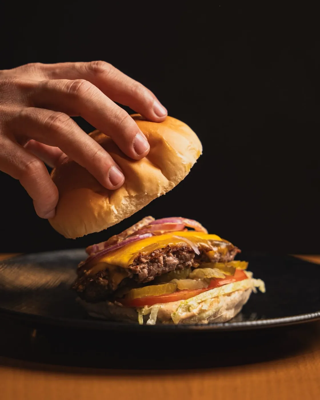 A hand placing the top bun on a Husk cheeseburger