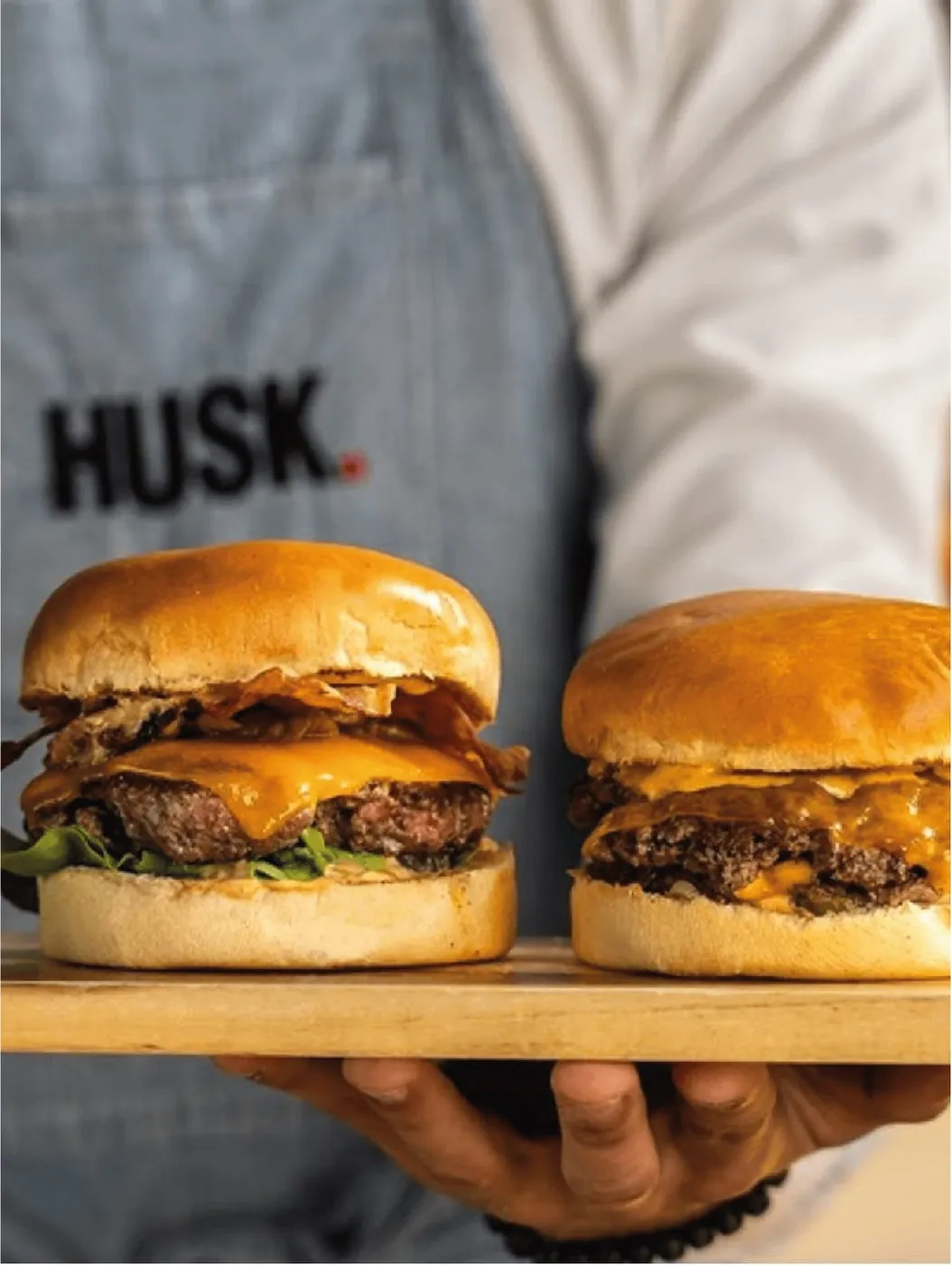 Two Husk burgers on a board, held by a member of the team