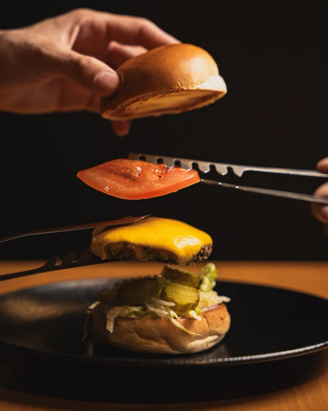Tongs placing a tomato slice on a burger